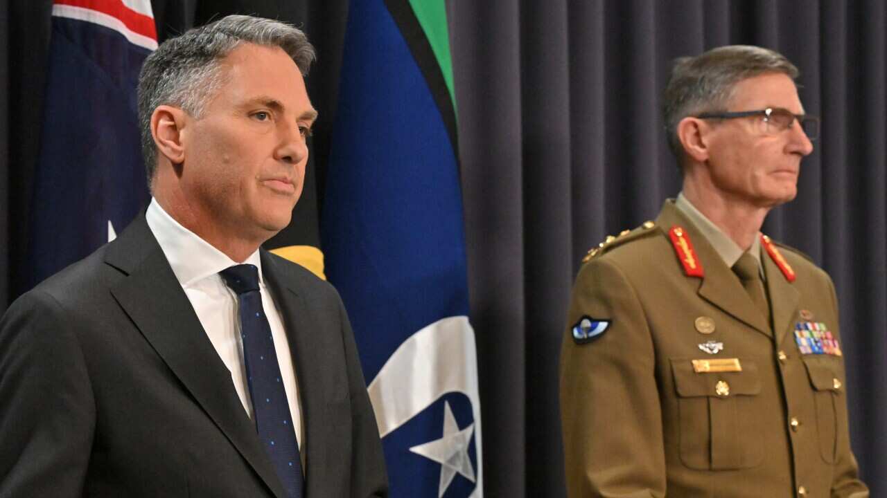 Two men wearing formal attire standing at lecterns in front of microphones.