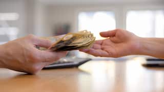 Hands exchanging Australian banknotes in a cash payment.
