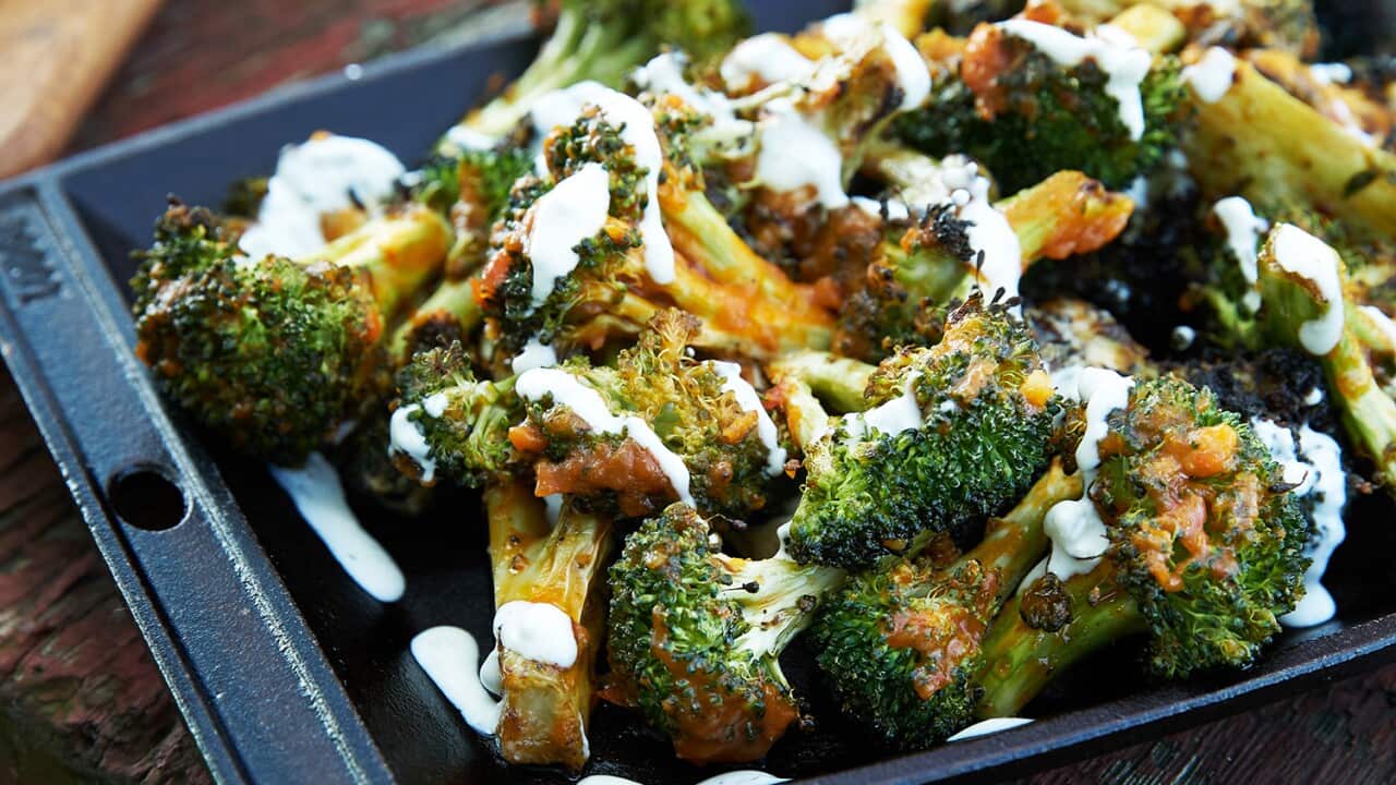 Cooked broccoli florets sit in a cast iron tray, drizzled with a brown sauce and a creamy sauce.