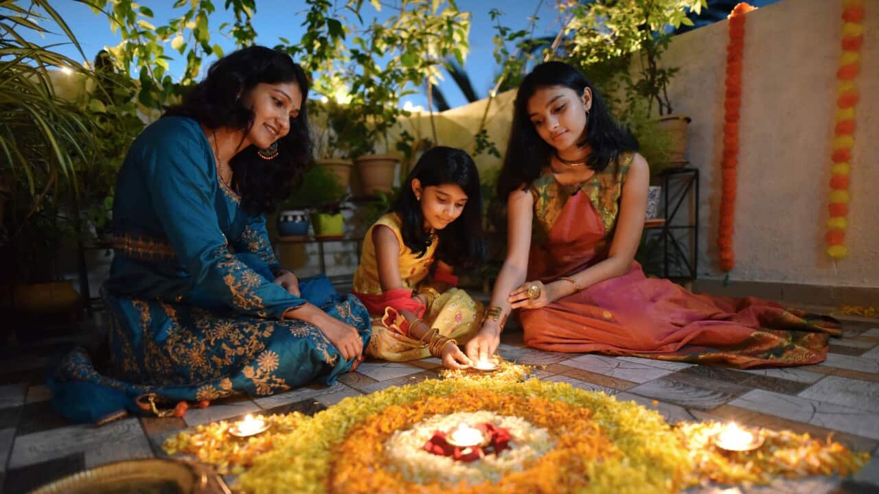 Mother and daughters lighting lamps around rangoli made using petals