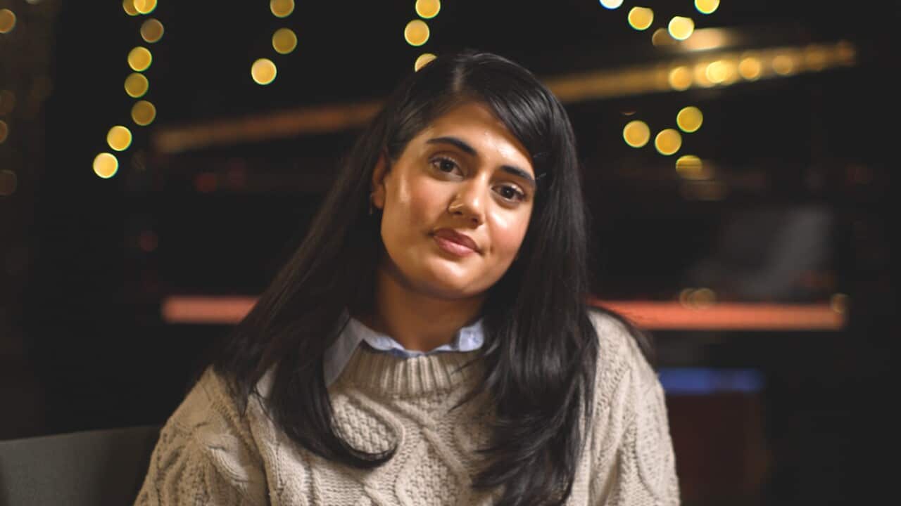 Young Indian-Australian actress Ayesha Madon from Heartbreak High sits in a dimly lit study with fairy lights in the background and looks to camera