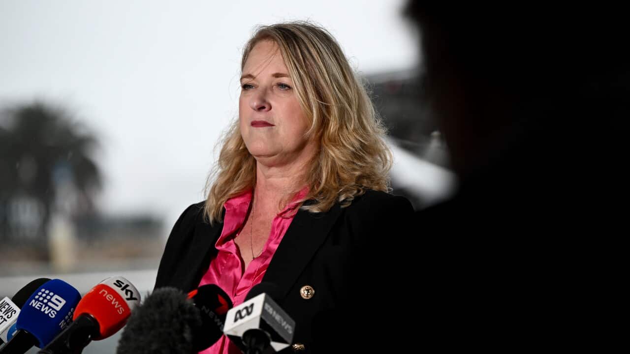 A woman wearing a black jacket and pink shirt looks on at a presser