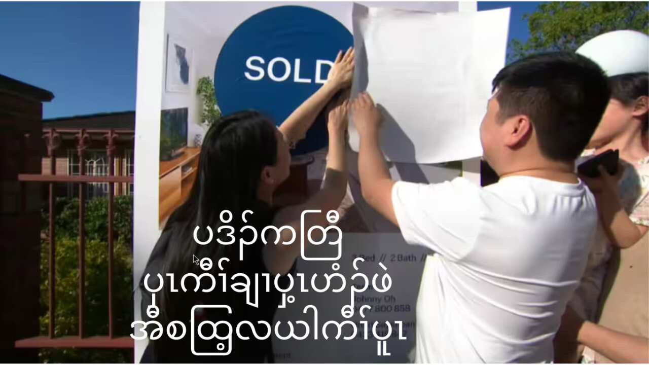Couple peeling back SOLD sign on property (SBS)