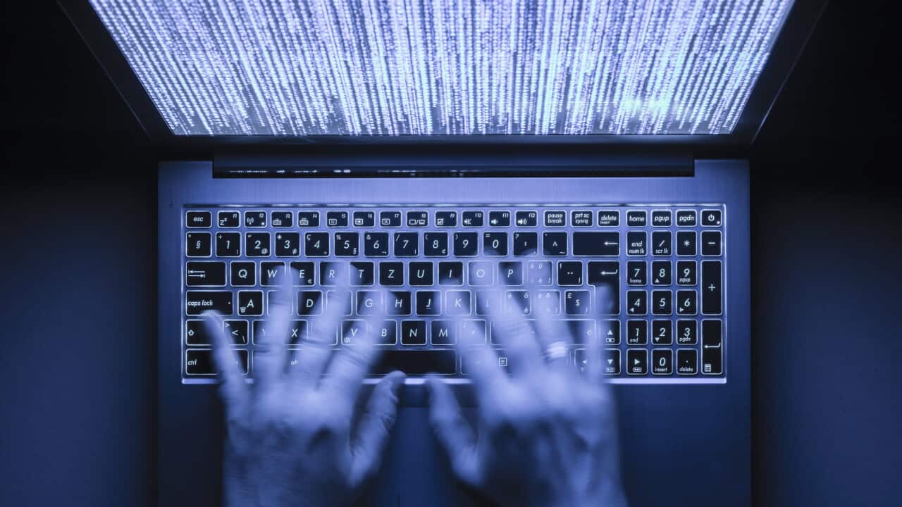 Hands typing on a laptop in the dark. Program code is visible on the screen.