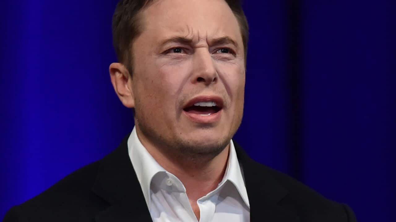 A man in a suit talks on stage with his hands open.