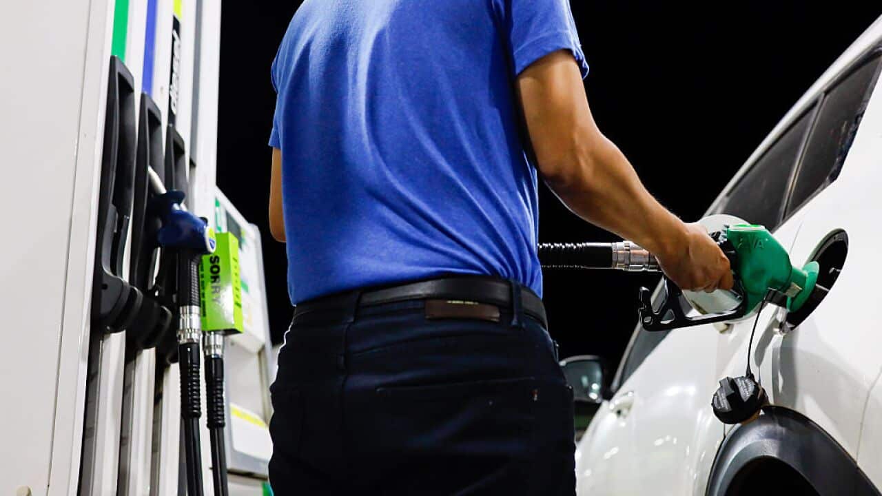 A man in a blue shirt fills his car with petrol at a petrol station