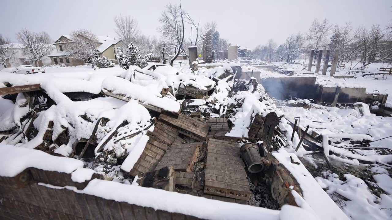 The remains of a home destroyed by a pair of wildfires is draped by snow