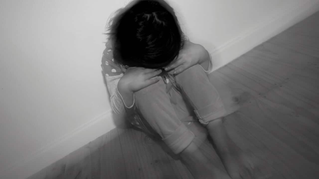 A young girl sitting in a corner of a room