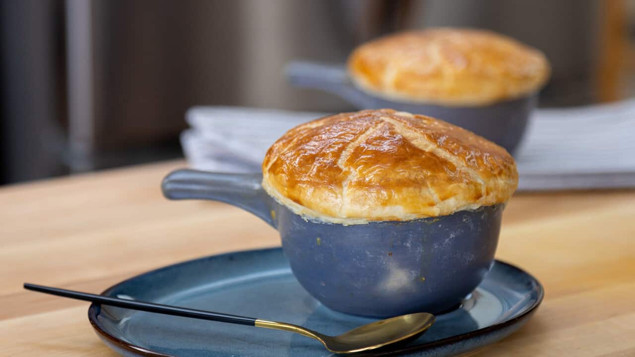 Sitting on a matching plate, a blue pottery bowl with a handle is covered with a cap of pastry. Another can be seen in the background.