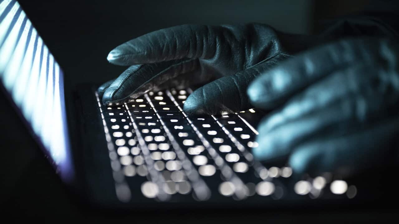 A person types with gloved hands on an illuminated laptop keyboard.