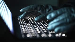 A person types with gloved hands on an illuminated laptop keyboard.