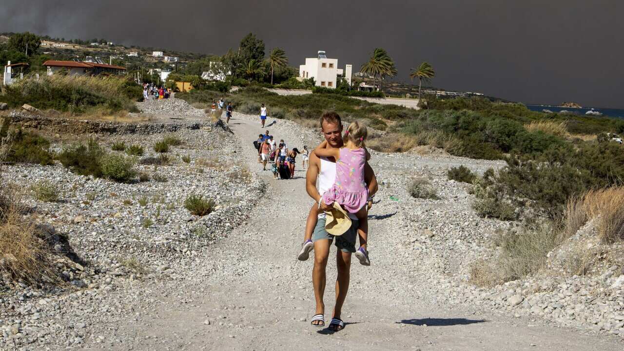 A man in shorts carries a young girl while he walks down a hill, with a smoky sky in the background.