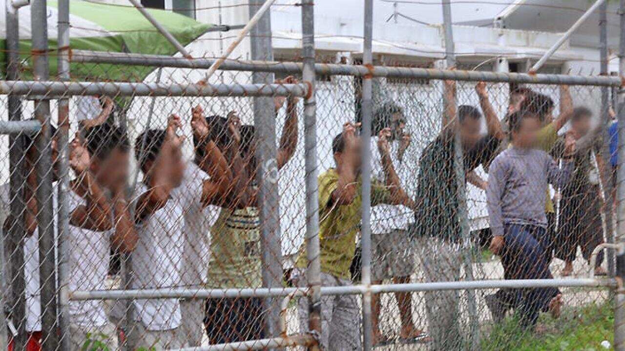 Asylum seekers staring at media from behind a fence at the Manus Island detention centre