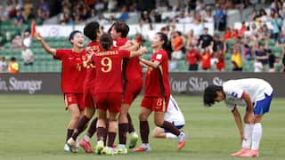 A photo from the 2026 Women's Asian Cup quarter finals. Chinese players dressed in red and gold kits celebrate their hard-fought 2-0 win over Taipei. Two Tapei players nearby are dressed in blue and white kits and appear dispirited by the loss.