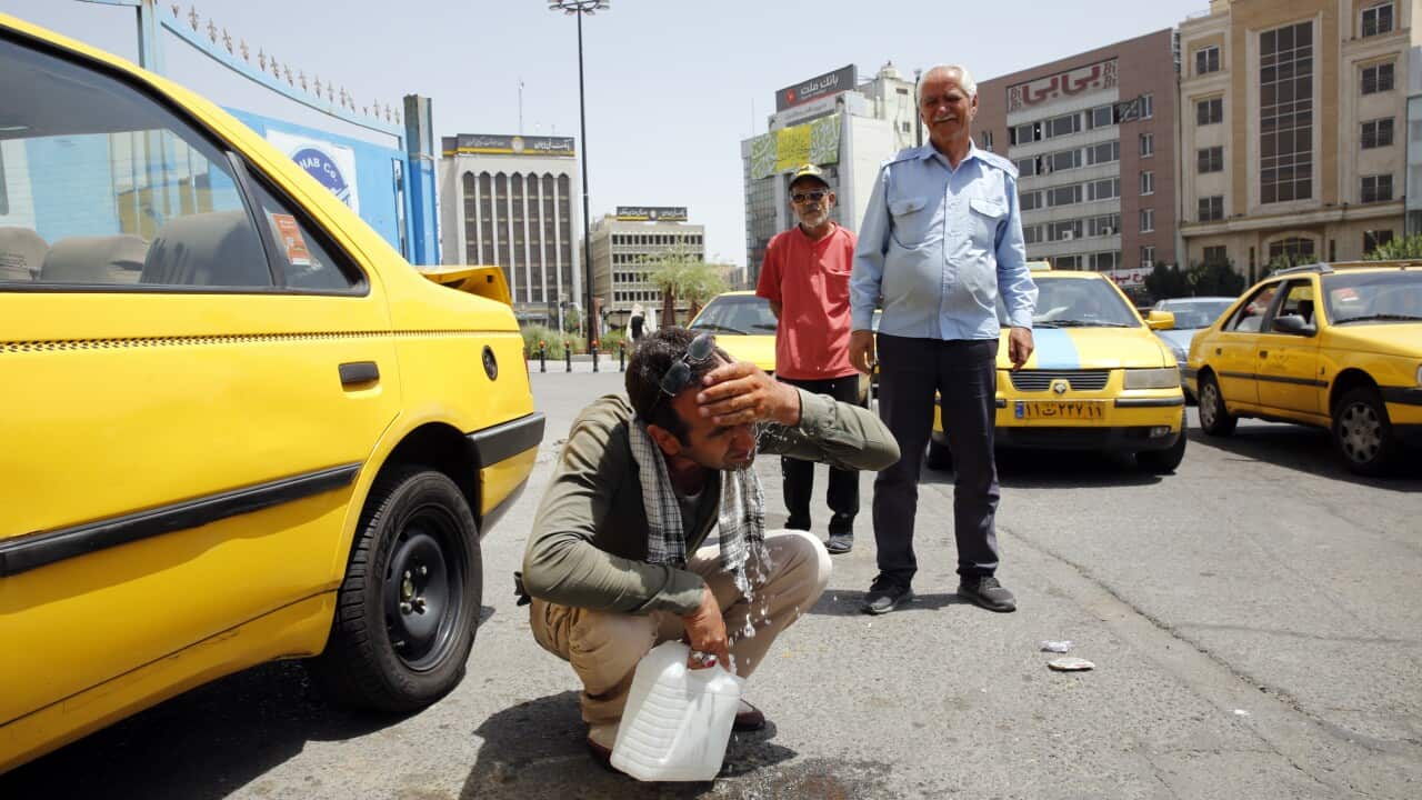 A man squats on the ground to wash his face next to a car as two others look on