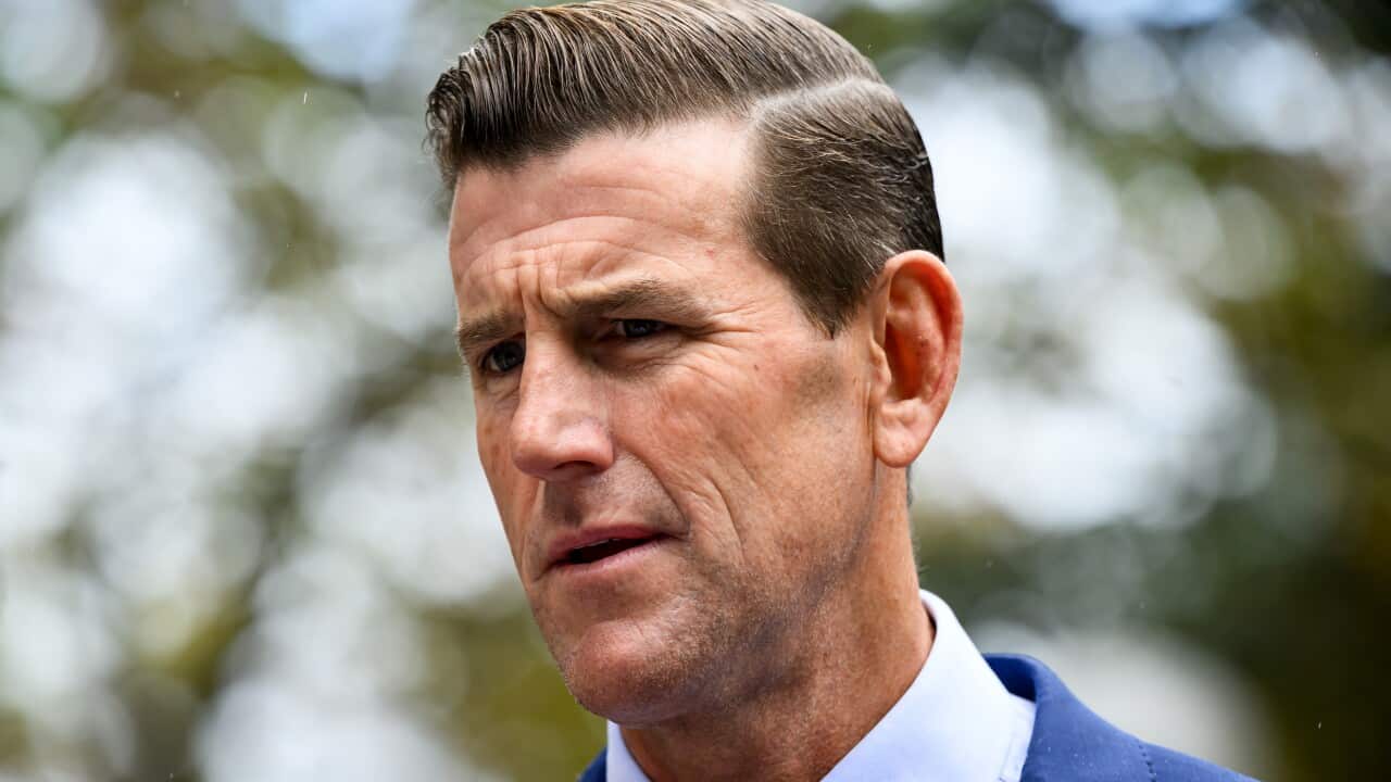 Ben Roberts-Smith, wearing a blue suit, standing in front of trees.