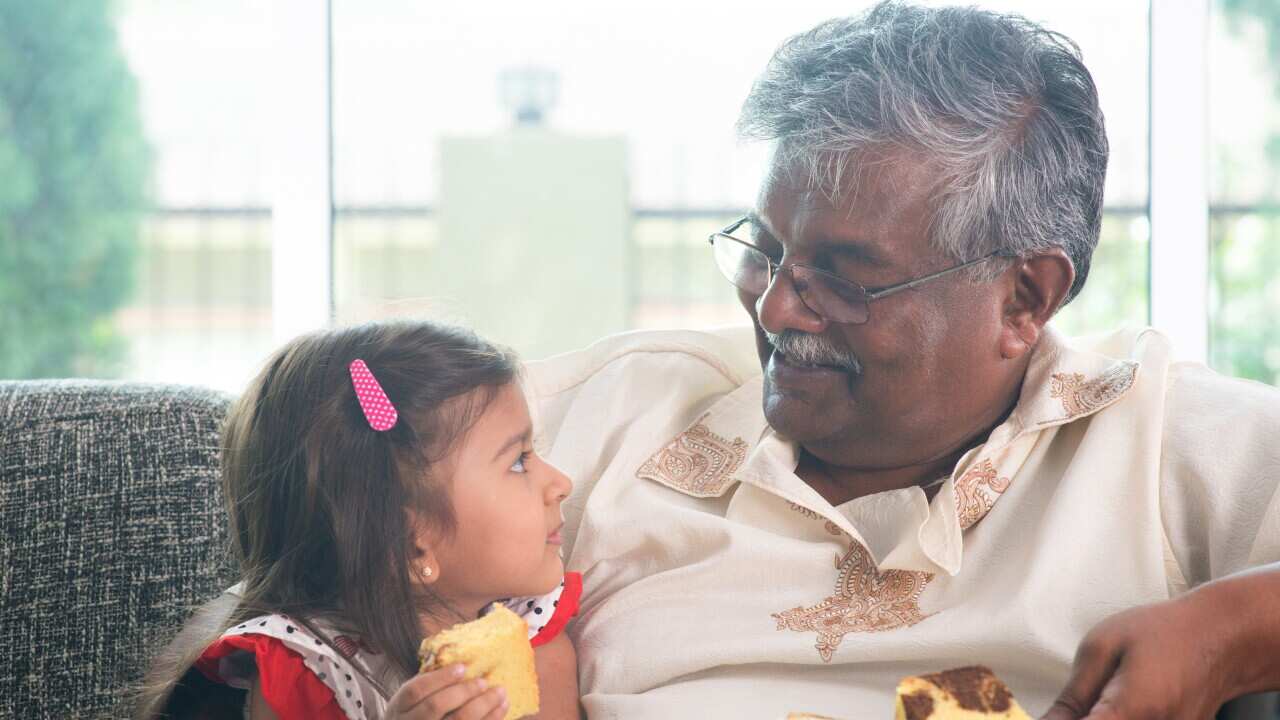 Granddaughter And Grandfather Having Sweet Bread On Couch At Home