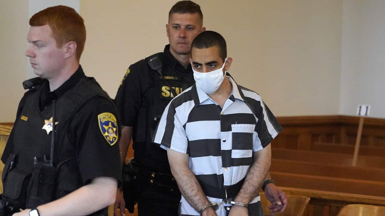 A man wearing handcuffs is escorted by two police officers.