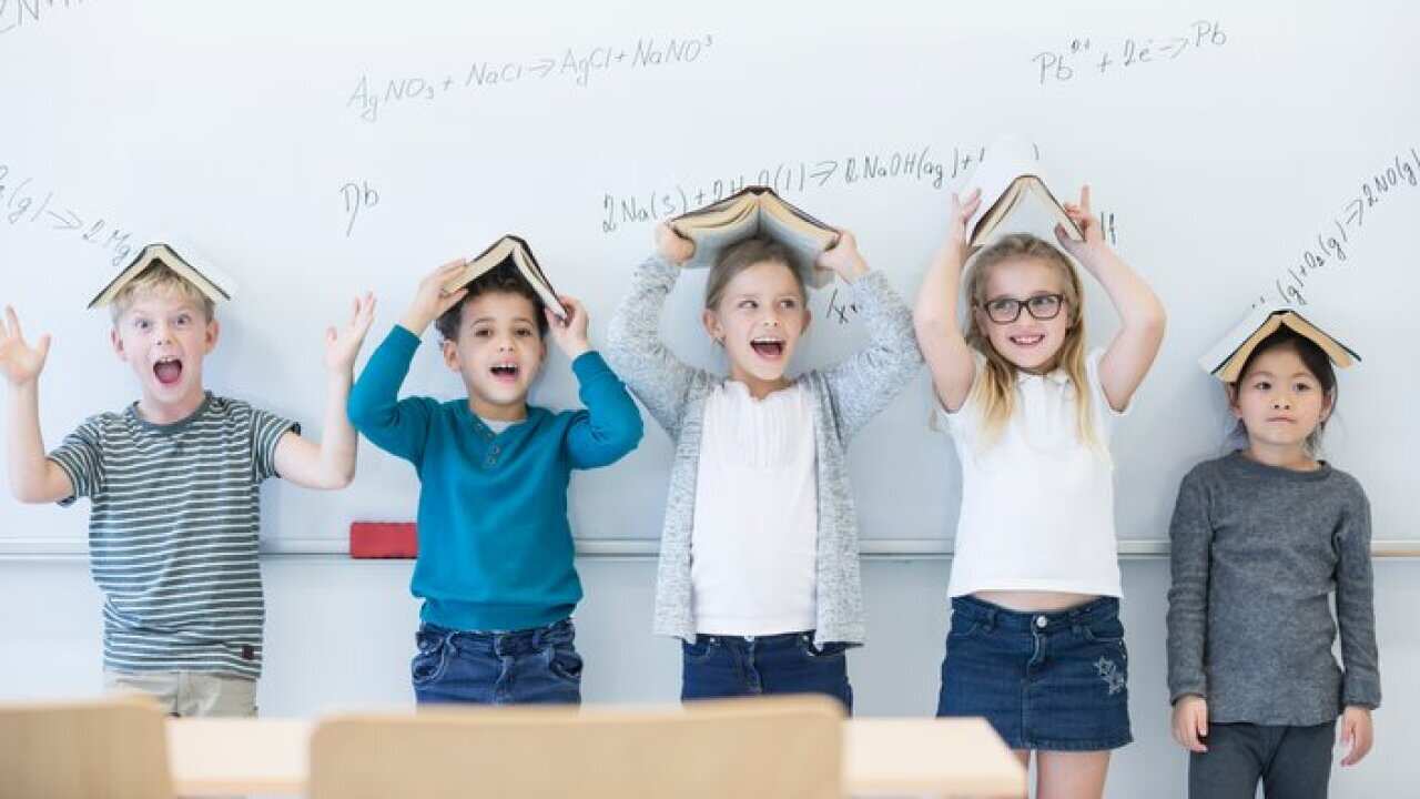 Happy pupils with books above their heads