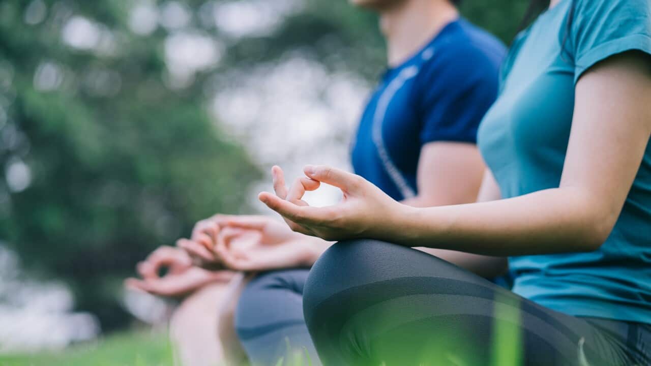 Image of young Asian couple meditating together on the grass
