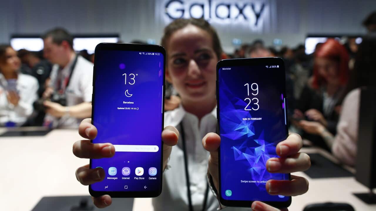 A woman at a Samsung Galaxy store carrying two S9 models facing outwards