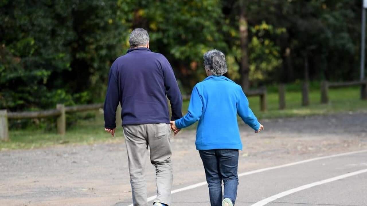 An elderly couple walk through a park