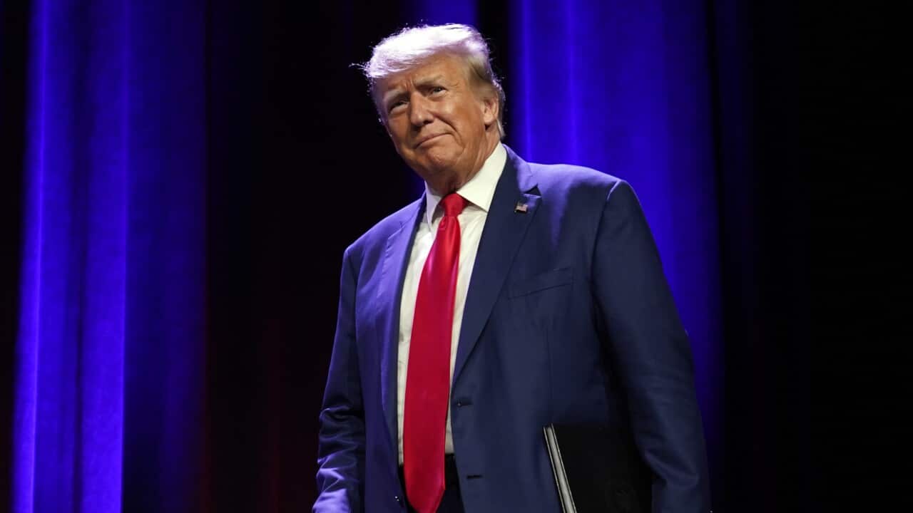 Wearing a dark blue suit and red tie, Donald Trump walks across a stage