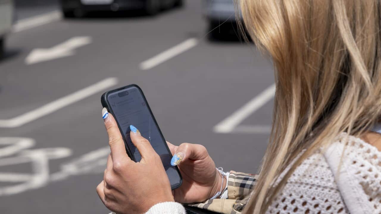 A woman browsing her smart phone besides a road
