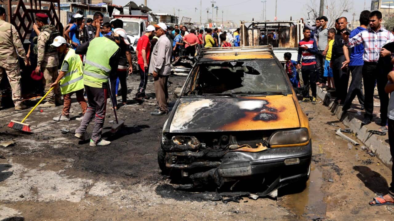 Workers clean up while civilians inspect the site of a car bomb attack