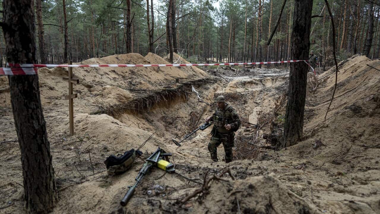 A Ukrainian serviceman uses a metal detector to inspect a mass grave in the recently retaken area of Izyum, Ukraine.