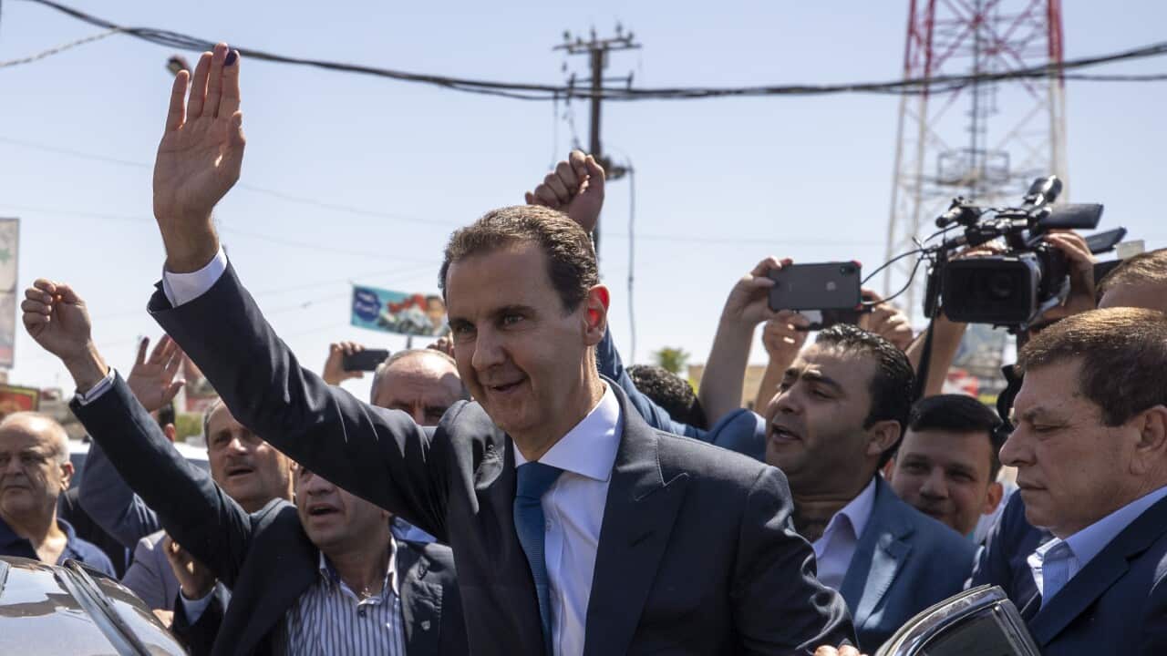Syrian President Bashar Assad, center, waves to his supporters at a polling station in the town of Douma