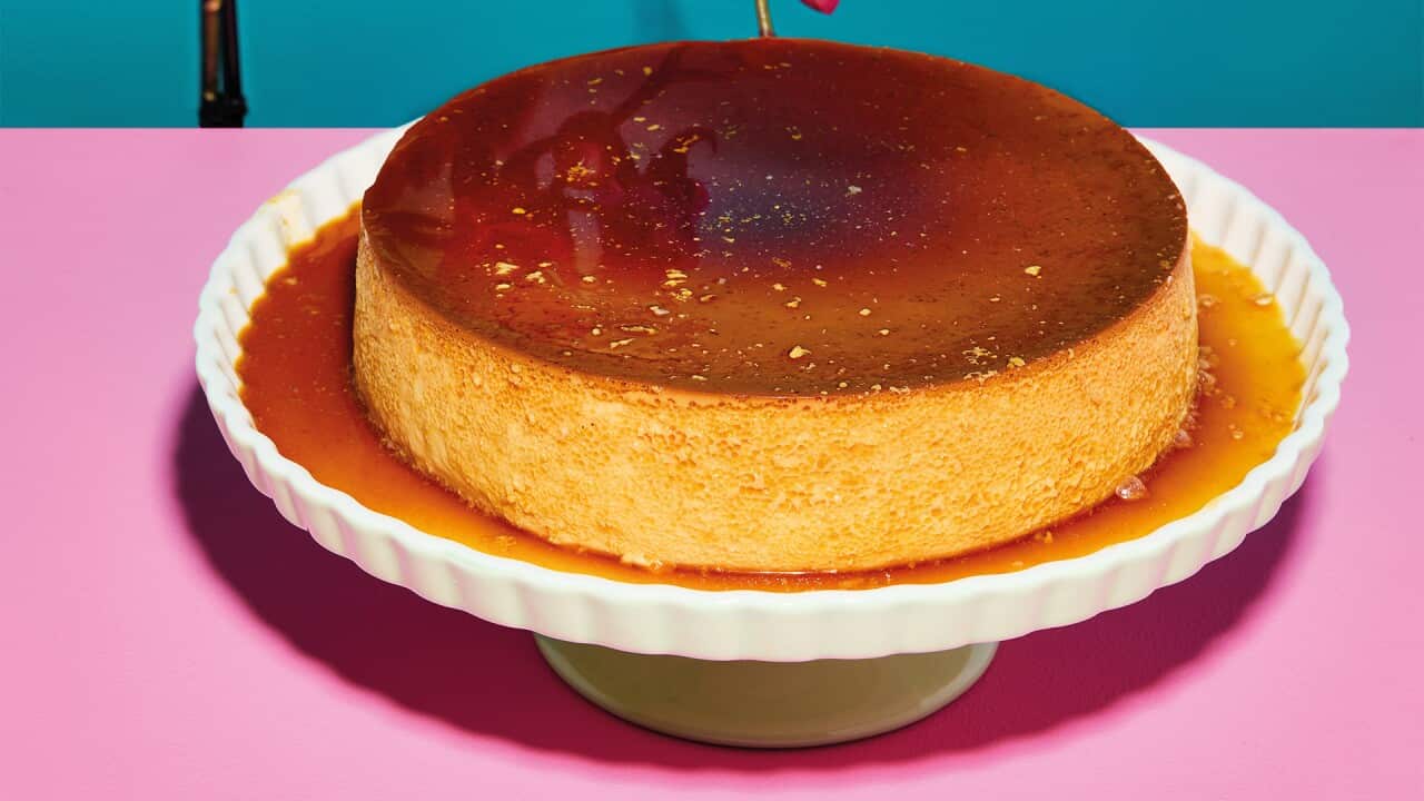 Banana Milk Flan sits in a pool of caramel on a white cake stand.