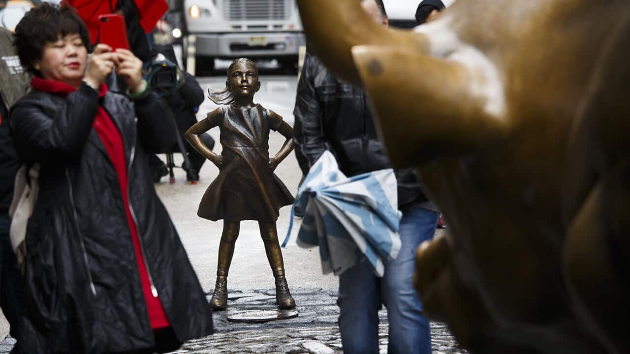 People are seen around a sculpture titled 'The Fearless Girl' by artist Kristen Visbal in New York
