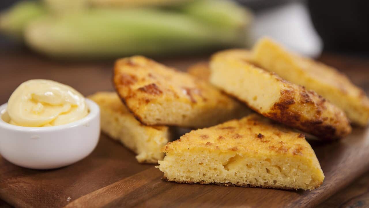 Wedges of golden cornbread sit on a wooden board beside a small dish of butter.