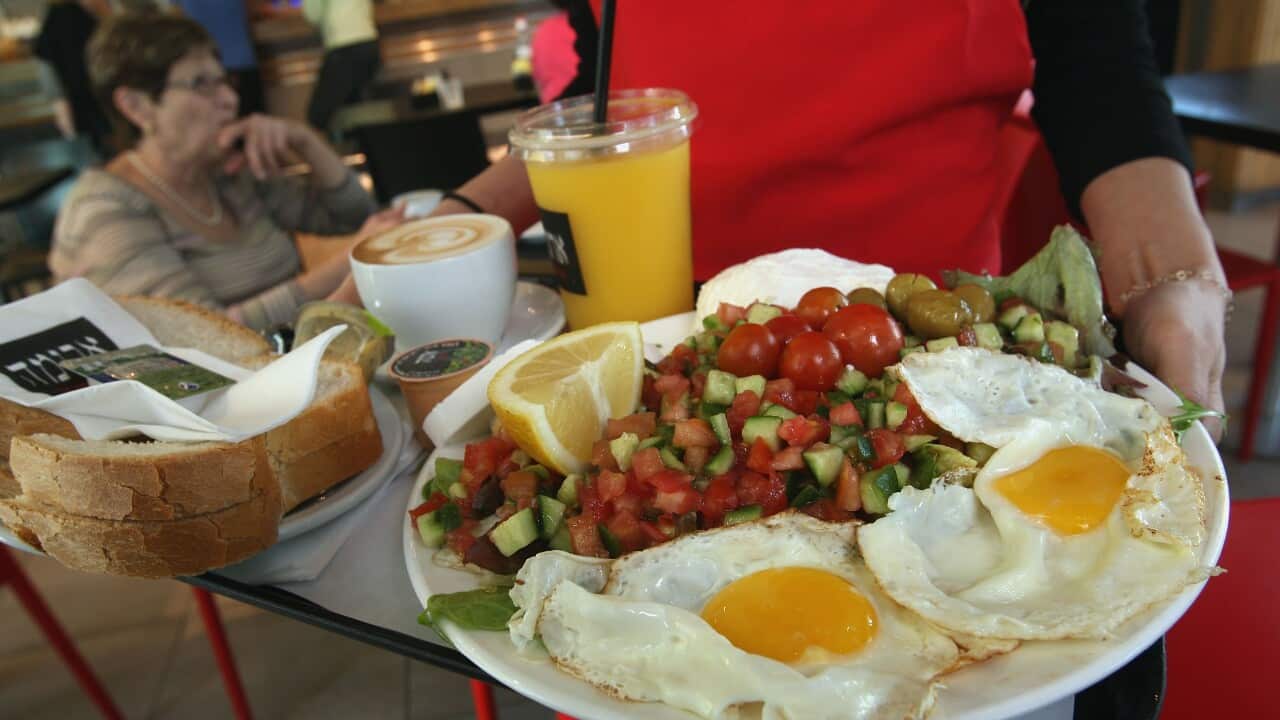 A waitress serves breakfast for two, including eggs, cheeses, salad, orange juice, coffee and fresh-baked bread.