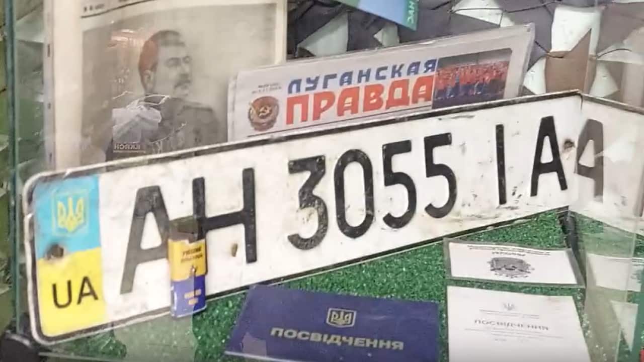 A few items are displayed inside a glass cube: a Ukrainian license plate, two Ukrainian newspapers, and some documents.