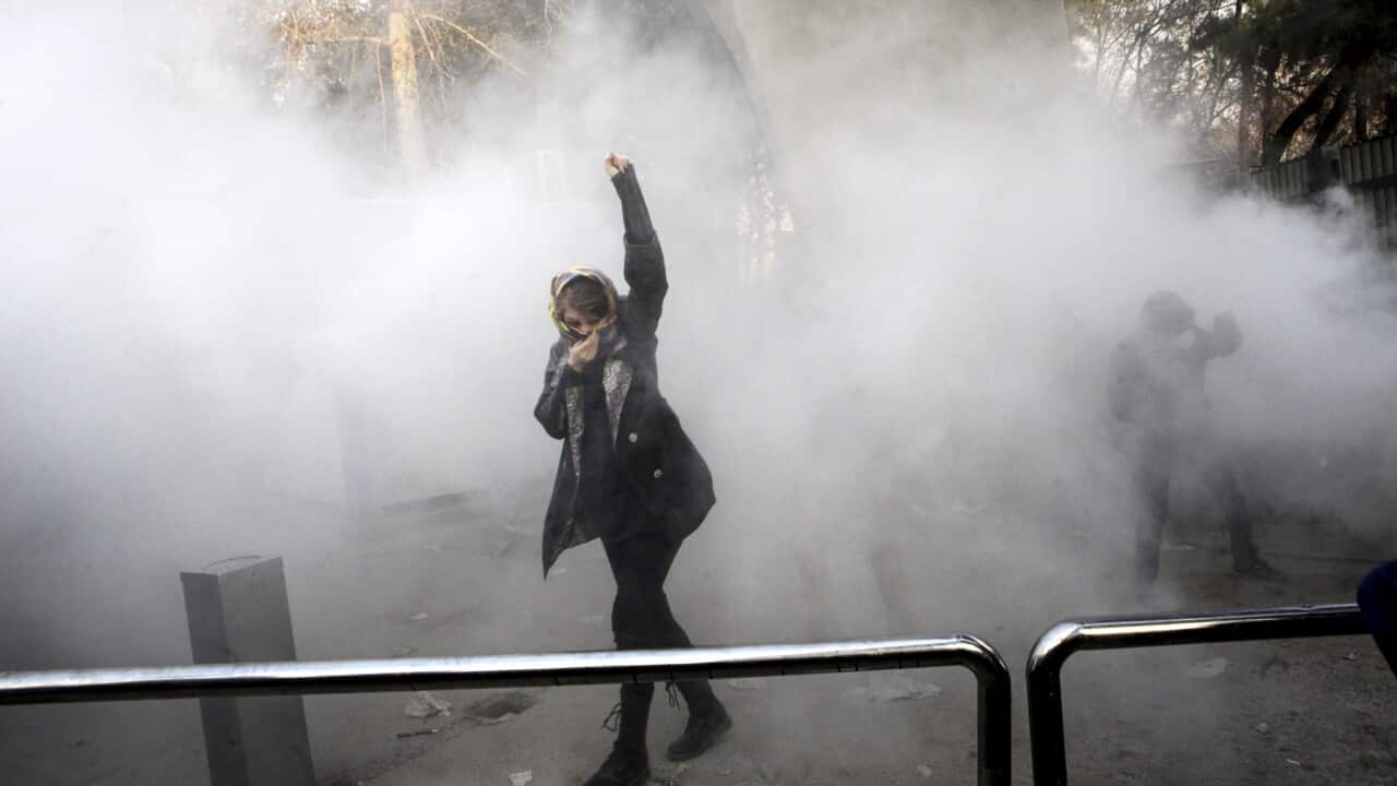 A student attends a protest inside Tehran University while a smoke grenade is thrown by anti-riot police.