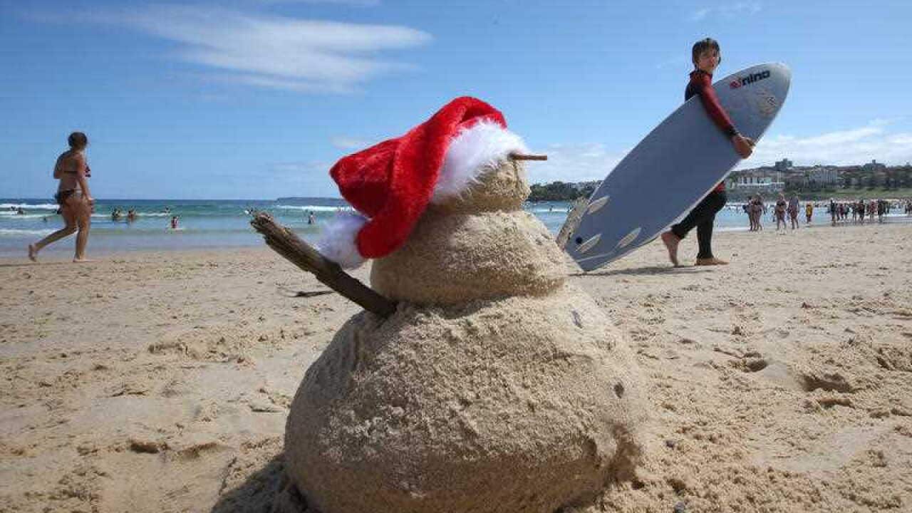 A young surfer walks past a snowman made of sand while celebrating Christmas Day on Bondi Brach in Sydney, Australia, Friday, Dec. 25, 2015.