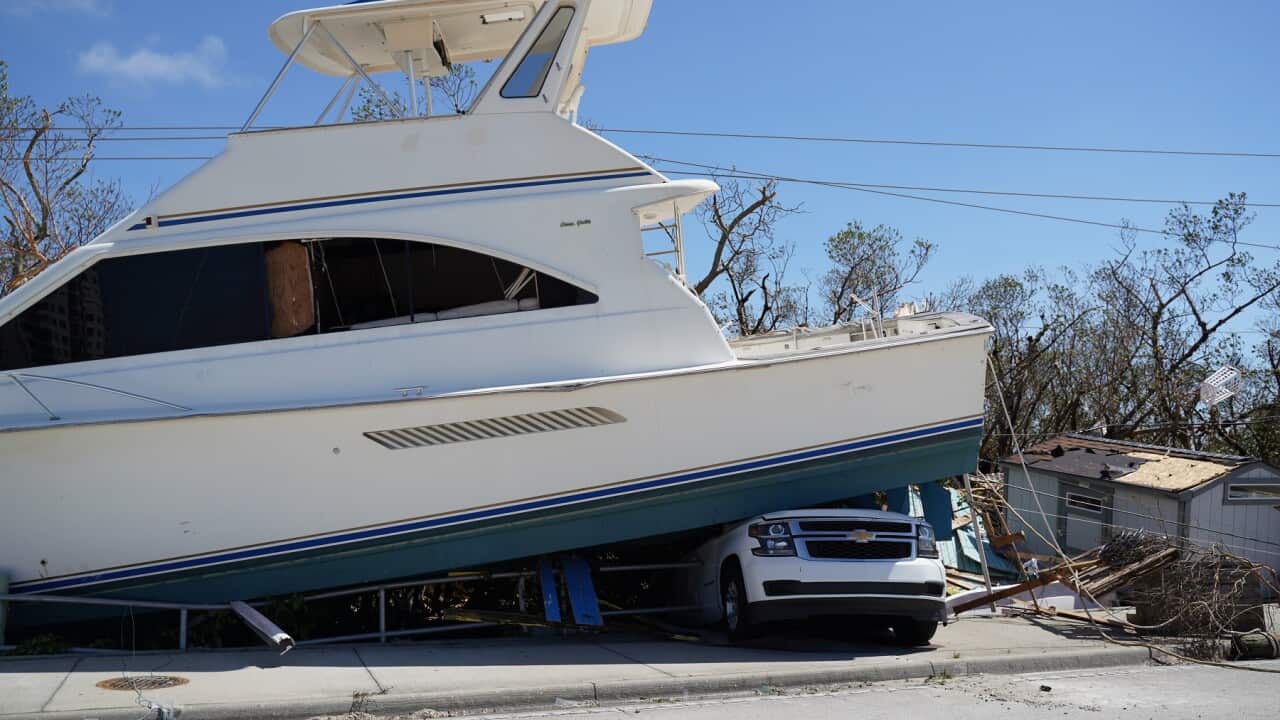 A boat sitting on top of a car with debris of a house next to it.