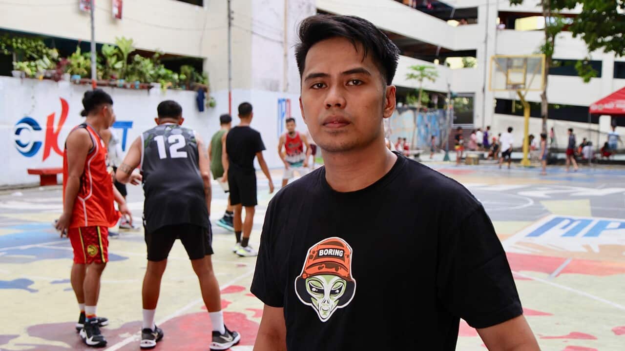 Man standing on a colourful basketball court with players in the background.