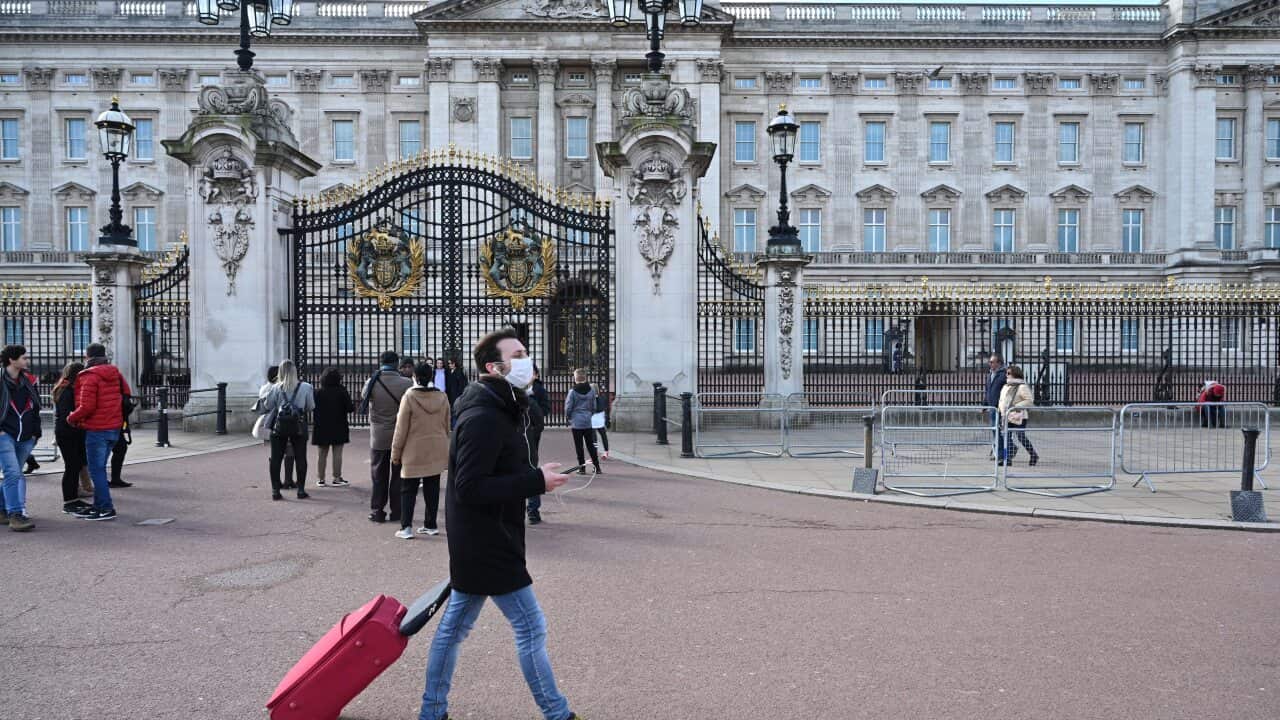 A man in a surgical mask passes an unusually small crowd outside Buckingham Palace in London, Britain.