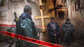 A montage featuring an armed security officer and a large gold cross superimposed over two men sitting in an alleyway in the Old City of Jerusalem, bisected by red police tape.