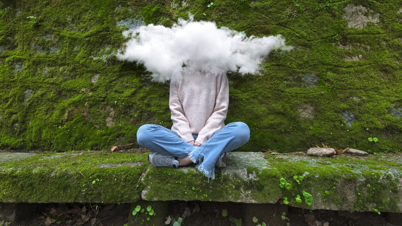 Young and timid woman with head in the cloud sitting on bench