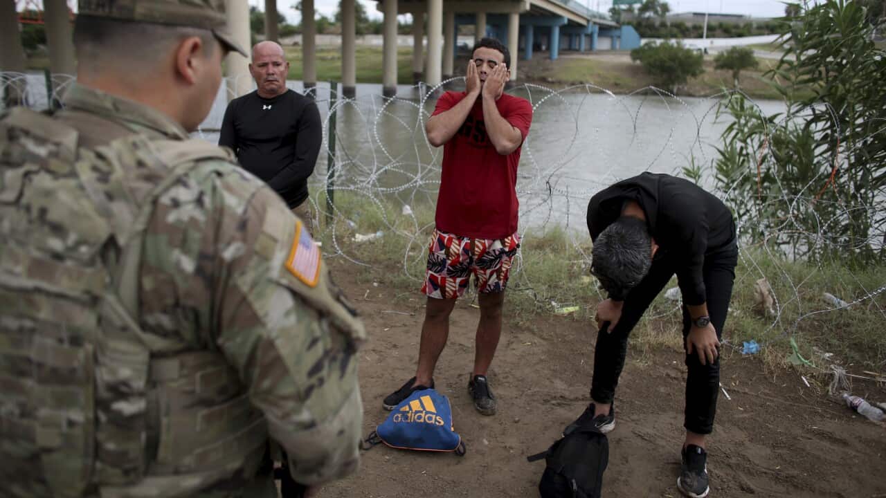 Three migrants from Cuba stand oil front of a National Guardsman after crossing the Rio Grande river in Eagle Pass, Texas.
