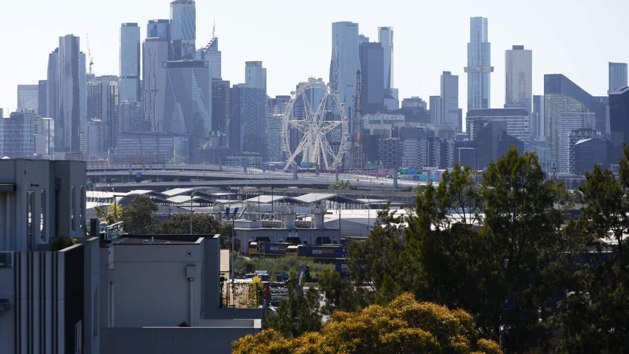 People on the street gaze up at multiple severely fire-damaged buildings as smoke rises