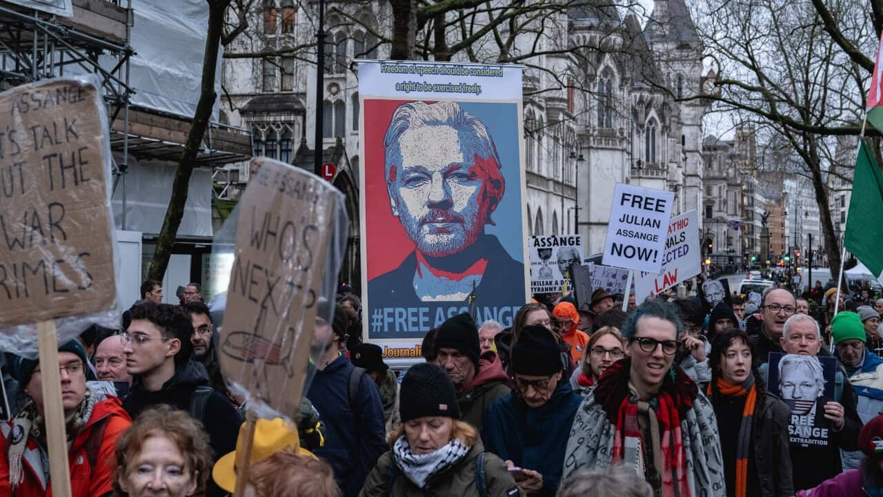 A crowd of supporters and protesters marching for Julian Assange's freedom with signs.