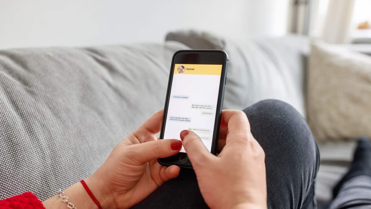 A woman holding a mobile phone in front of her with a social media chat screen open.