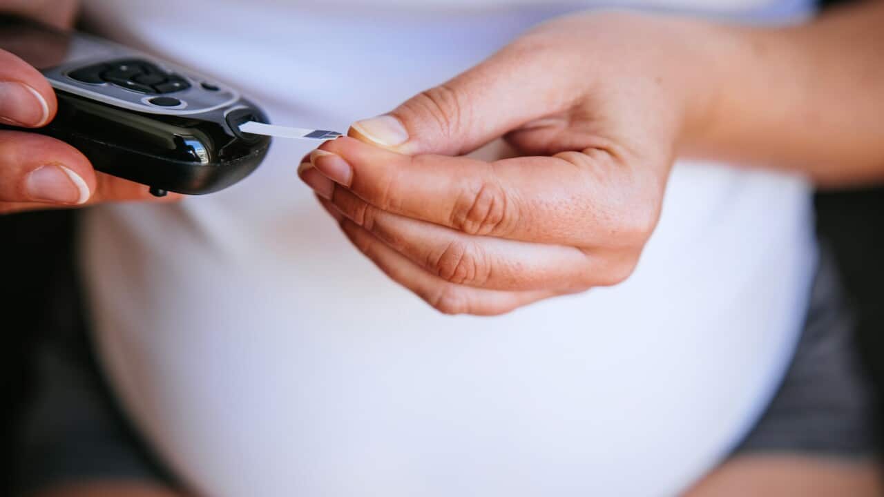 Pregnant woman is using a glucometer at home.