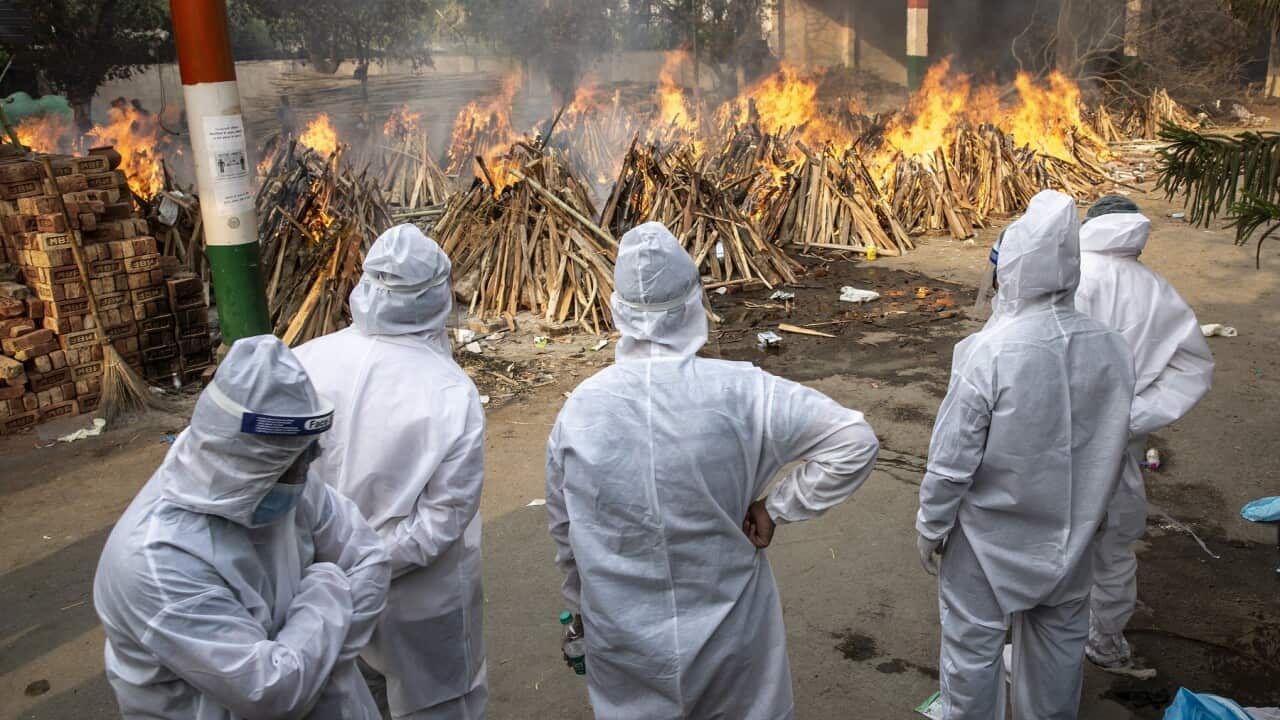 Visitors dressed in PPE suits watch at a cremation site in New Delhi