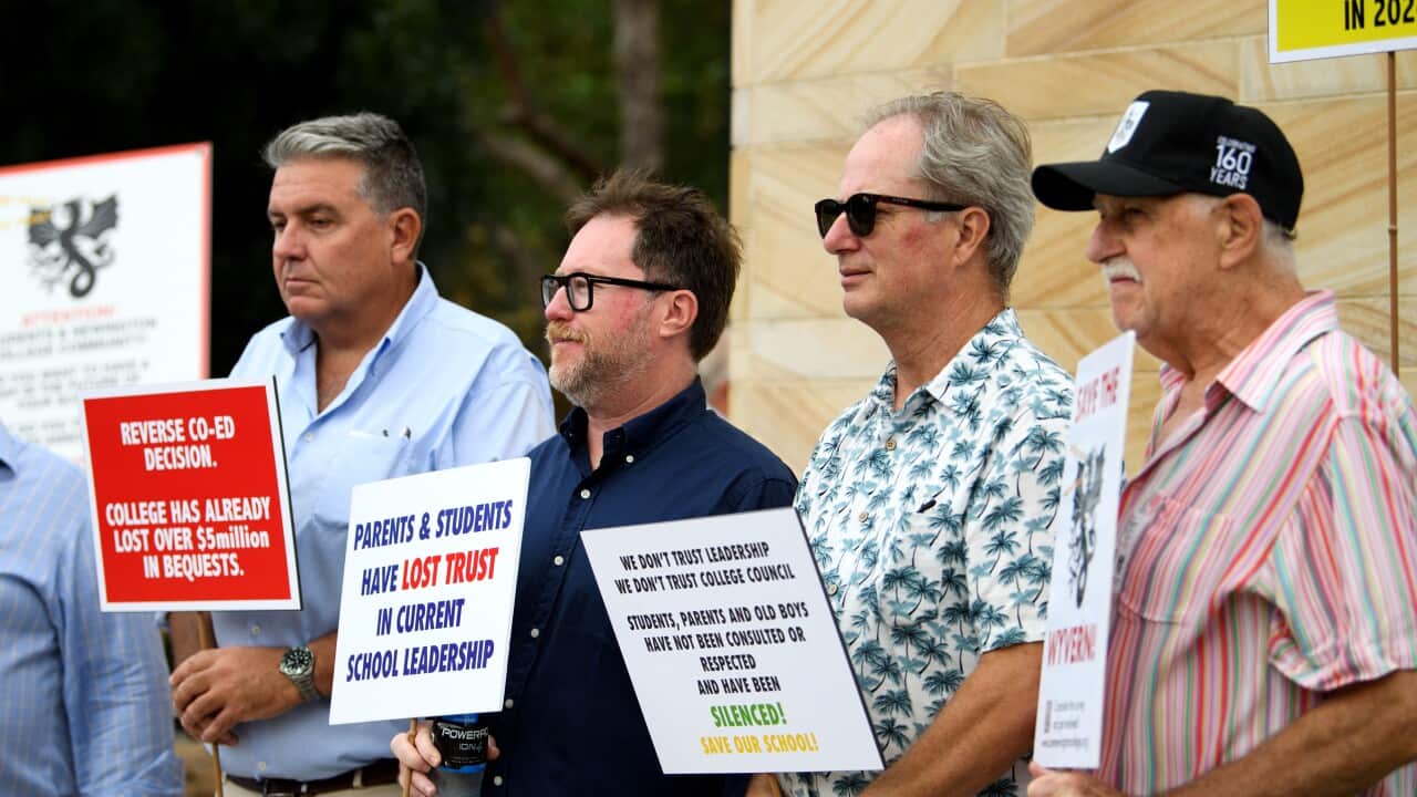 Men standing in a line outside and holding placards during a protest